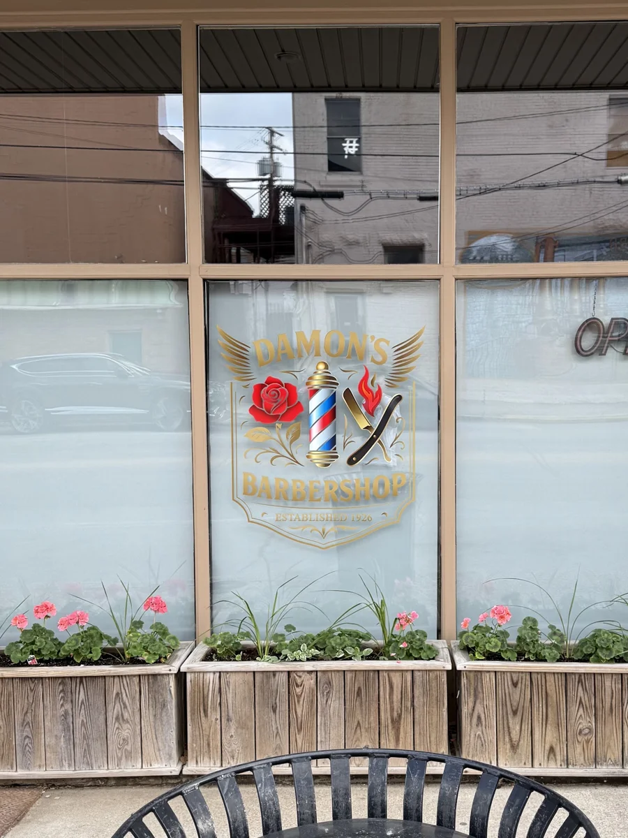 Damon’s Barbershop mark on the Lexington Street shop window above flower boxes