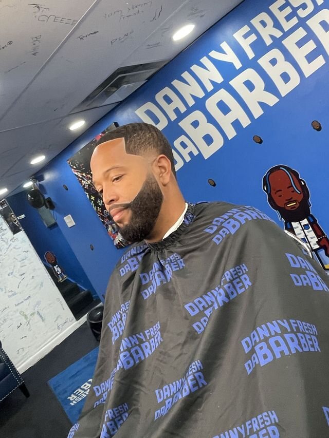 Danny Fresh haircut and beard with the shop's blue wall behind